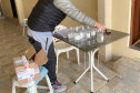 Pessoa recolhendo frascos de alcool em gel sobre uma mesa