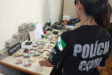 Policial civil em frente a uma mesa com drogas, objetos e dinheiro apreendidos