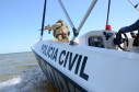Policial civil na proa do barco da polícia civil, apontando arma
