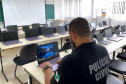 Laboratório de informática. De costas, em primeiro, plano, policial ao computador.