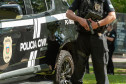 Policial civil ao lado de viatura empunhando arma