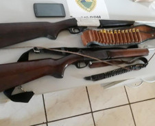 Duas armas, munição e um celular apreendidos, sobre uma mesa