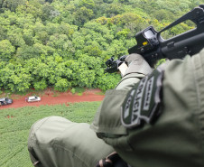 Policial civil em helicóptero apontando fuzil para abordagem terrestre