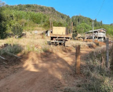 Estrada de terra cercada por vegetação, com um caminhão e uma construção