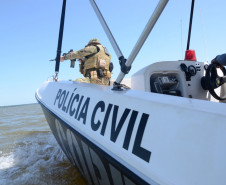 Policial civil na proa do barco da polícia civil, apontando arma