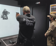 Policial aponta arma para alvo no simulador, observado pelo instrutor