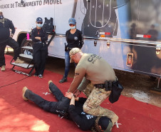 Policiais civis observam técnicas de algemamento, ao lado de caminhão simulador