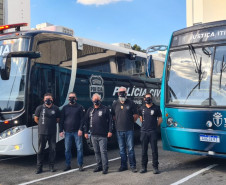 Policiais civis posando para foto entre ônibus da PCPR e TJ