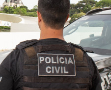 Policial civil de costas, ao lado de viatura