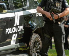 Policial civil empunha arma ao lado de viatura