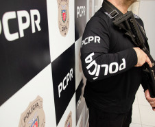 Policial civil empunhando arma ao lado de banner da PCPR
