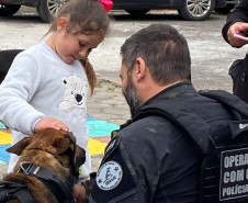 Policial civil acompanha criança acariciando cão policial