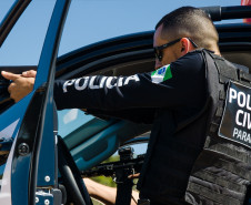 Policial civil apontando arma ao lado de veículo