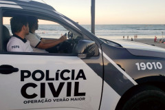 Dois policiais civis no interior de uma viatura, no litoral.