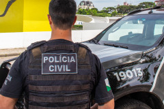 Policial civil, de costas, ao lado de viatura