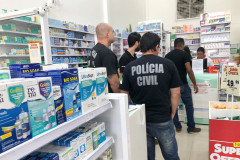 Policiais civis de costas, no interior de uma farmácia