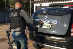 Policial civil abrindo tampa do porta-malas do carro para retirar suspeito