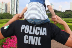 Policial civil segurando as mãos de criança que está sobre os ombros dele.