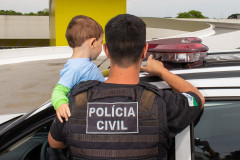 Policial civil segurando criança no colo, mostrando giroflex de viatura