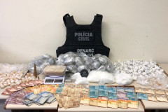 Colete da Polícia Civi, drogas, balanca e cédulas de dinheiro sobre uma mesa