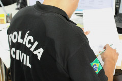 Policial civil sentado, de costas, averiguando documento