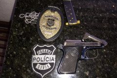 Arma apreendida e distintivos da polícia, sobre uma mesa