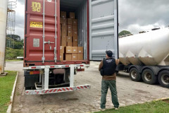 Policial civil segura porta do baú de caminhão e observa material recuperado