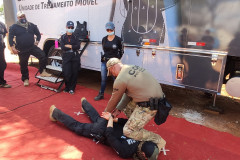 Policiais civis observam técnicas de algemamento, ao lado de caminhão simulador