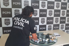 Policial civil de costas, reunindo material apreendido sobre uma mesa
