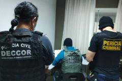 Três policiais civis de costas, analisando documentos