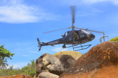 Helicóptero da policia civil levantando voo no litoral. Diversas rochas em primeiro plano.