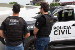 Dois policiais civis ao lado de viatura