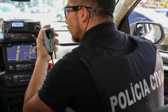 Policial civil de costas, falando pelo rádio, dentro de viatura