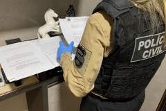 Policial civil em pé, analisando documentos