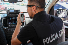 Policial civil falando pelo rádio, dentro de uma viatura