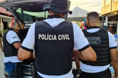 Policiais civis de costas, com tampa de porta-malas de viatura aberta