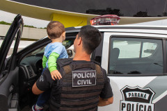 Policial civil aparece com criança no colo ao lado de viatura.