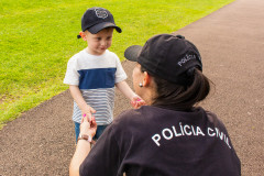 Policial civil interage com uma criança, ambos com bonés da polícia