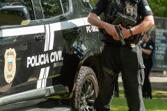 Policial civil ao lado de viatura empunhando arma