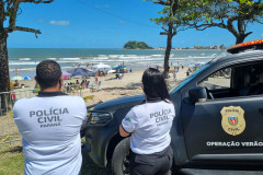 Dois policiais civis ao lado de viatura observam movimento na praia