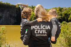 Policial civil com duas crianças no colo observam lago e cachoeira no parque Tangua