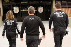 Três policiais de costas entrando em delegacia