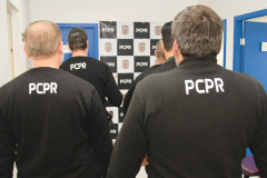 Vários policiais civis de costas. Ao fundo, banner da PCPR