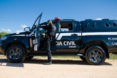 Policial civil ao lado de viatura apontando arma