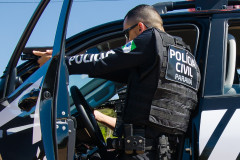 Policial civil apontando arma ao lado de viatura