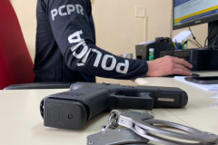 Policial civil ao computador. Em primeiro plano, arma e algemas