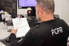 Policial civil ao computador lendo documento