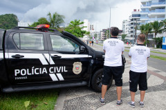 Dois policiais civis ao lado de viatura observando o movimento no litoral