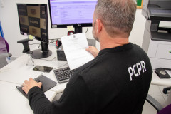 Policial civil ao computador observa documento
