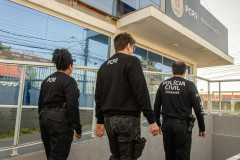 Três policiais civis saindo de delegacia